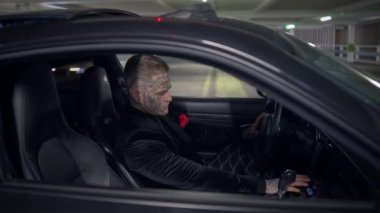 Loş bir otoparkta, gizemli bir figür şık bir arabada oturur, entrika ve gerilimi somutlaştırır.