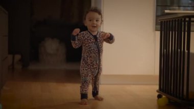 Neşeli ve neşeli, neşeli pijama giymiş bir çocuk sıcak ve rahat bir evde mutlu bir şekilde yürüyor.