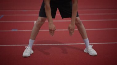 Canlı spor kıyafetleri giymiş bir atlet renkli bir koşu pistinde başlangıç pozisyonunda.