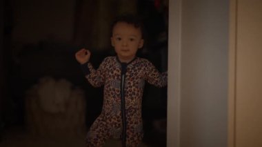 Leopar desenli pijama giymiş, küçük tatlı bir çocuk kapının önünde duruyor.