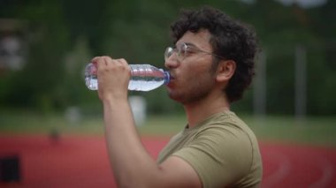 Genç bir adam ferahlatıcı bir mola vermek için mola verir ve canlı kırmızı bir atletizm pistinde antrenman yaparken kendini su kaybına uğratır.