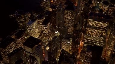 Parlak şehir gökdelenlerinin parlayan ışıklarıyla canlı şehir manzarasını gösteren, gece aydınlık gökdelenlerinin havadan çekilmiş fotoğrafı.