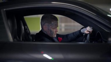 Eşsiz dövmeleri olan gizemli bir insan şık bir arabada oturuyor, entrika ve modern stil atmosferi yaratıyor.