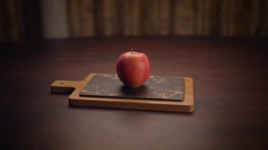 Kırsal ahşap bir kesme tahtasının üzerinde duran güzel canlı kırmızı bir elma, çeşitli mutfak temaları için ideal.