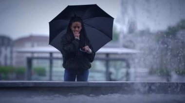 Renkli bir şemsiyenin altında, yağmurlu bir şehir sokağının ortasında düşünceli bir şekilde duran yalnız bir insan.