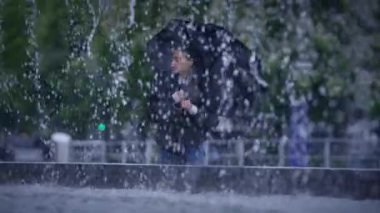 Canlı bir şemsiyesi olan yalnız bir figür çeşmenin kenarındaki sakin yağmurun tadını çıkarıyor, güzelliği kucaklıyor.