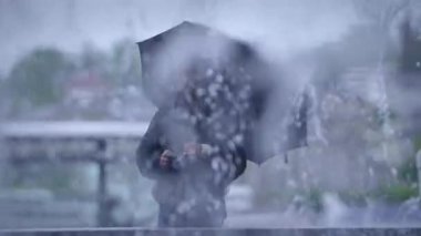 Şiddetli yağmurla çevrili bir şekilde şemsiye tutan yalnız bir figür, belirgin bir karamsar atmosfer yaratıyor.