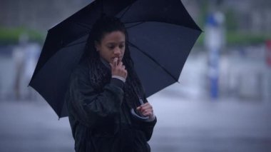 Düşünceli bir kadın, yağmurlu bir şehir zeminine karşı düşünceli düşüncelerinde kaybolurken şemsiyesini tutar.