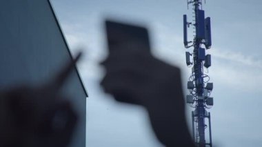 Akıllı telefonu olan bulanık bir insan silueti, arka planda hücresel iletişim kulesi.