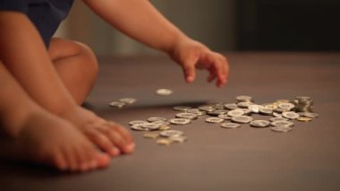 Genç bir çocuk sevinçle etrafı keşfediyor ve dağınık paralarla oynuyor pürüzsüz ahşap bir yüzeye yayılmış.