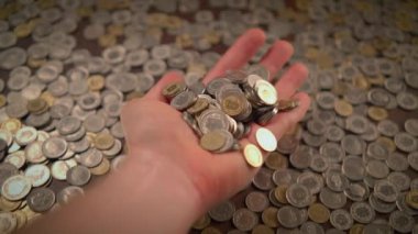 Bir el, maddi bolluğu sembolize eden, büyük bir bozuk para yığınıyla çevrili çeşitli paraları kavrıyor.