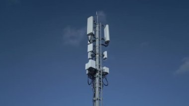 Çeşitli antenlerle donatılmış çağdaş bir telekomünikasyon kulesi açık mavi gökyüzüne karşı duruyor.