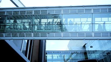 Modern bir şehir ortamında çarpıcı bir cam yaya köprüsünden geçen sayısız banliyö sakininin canlı ve canlı bir sahnesi.