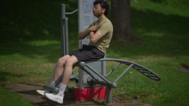 Genç bir adam açık hava fitness ekipmanlarıyla aktif olarak ilgileniyor. Doğadayken sağlıklı yaşam tarzlarını teşvik ediyor.