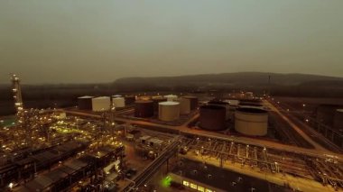 Hava kararırken endüstriyel petrol rafinerisinde büyük depolama tankları ve tesisleri gösteren panoramik bir çekim..