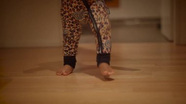 Neşeli bir çocuk ahşap bir zeminde rahat leopar desenli pijama giyerken neşeli hareketler sergiliyor.
