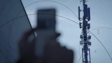 Akıllı telefon aynası, bulutlu bir gökyüzünün altındaki iletişim kulesini yansıtır ve modern teknolojiyi gösterir..