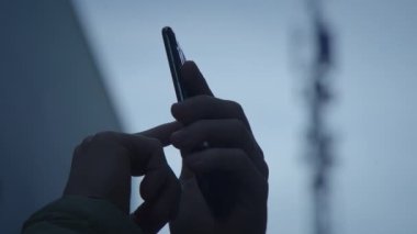 Akıllı bir telefonla iletişim kulesinin siluetine yakın çekim yapan bir el görüntüsü.