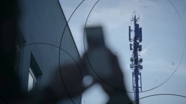 Akıllı telefonu tutan bir el, bir baz istasyonuna karşı siluetlenir. Teknoloji ve bağlantıyı gösterir..