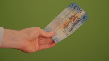Bir el, canlı yeşil bir zemin üzerine kurulmuş 1100 banknotu sıkıca kavrıyor. Bu da döviz kurunu net bir şekilde gösteriyor.