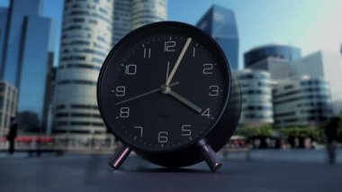 Pürüzsüz, modern bir siyah çalar saat, arka planda hareketli, hareketli bir şehrin siluetine karşı güzel bir tezat oluşturuyor.
