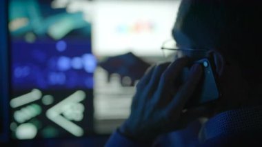 Bir teknoloji uzmanı, bir telefon görüşmesi sırasında çeşitli ekranları izler, modern çalışma dinamiklerini somutlaştırır..