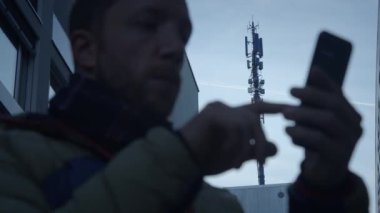 Kalabalık bir şehir ortamında, bir adam sokakta akıllı telefonuyla dikkatle iletişim halindedir.