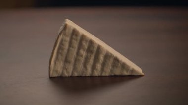 Tahta bir masada sergilenen üçgen bir zanaatkar peynirin yakın çekimi zengin dokusunu güzel bir şekilde sergiliyor.