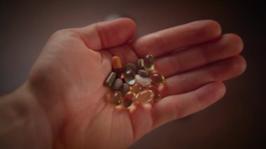 Çeşitli vitaminler, mineraller ve çeşitli şekillerde takviyeler içeren bir elin yakından görüntüsü.