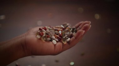 Bir el, çeşitli renkli hapları ve kapsülleri incelikle tutar. Koyu ahşap arka planda ustalıkla sergilenir.