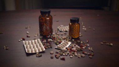 Çeşitli ilaç ve şişelerden oluşan bir derleme ahşap bir yüzeye yayılarak düzensiz bir sıra oluşturur.