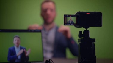 Profesyonel bir kamera ve monitör kurulumu ile donatılmış yeşil ekranın önünde bir konuşmacı kendinden emin bir şekilde sunum yapıyor