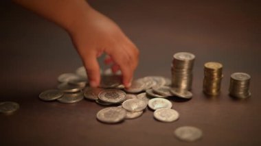 Küçük bir çocuk, finans, öğrenme ve büyümeyi temsil eden madeni para çeşitleriyle neşe içinde etkileşime girer.
