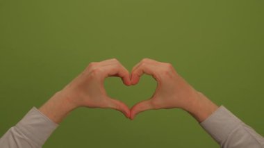 İki el bir araya gelerek güzel kalp şekilleri oluşturuyor. Canlı yeşil bir zemin üzerinde sevgi ve bağlantıyı simgeliyor.