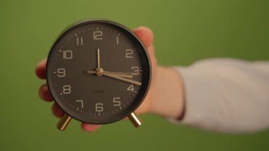 Çağdaş bir çalar saat, canlı yeşil bir arkaplan karşısında parlak tasarımını sergiliyor.