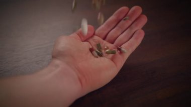 Yakın çekim görüntüsü, ahşap bir yüzey üzerinde çeşitli haplar ve besin takviyeleri içeren bir el ele gösteriyor.