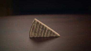 Koyu ahşap bir masa üzerindeki üçgen peynirin yakından görüntüsü, dokusunu güzelce vurgulıyor.