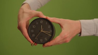 Zaman yönetiminin önemini vurgulayan, parlak siyah bir çalar saati sıkıca tutan ellerin yakın plan görüntüsü