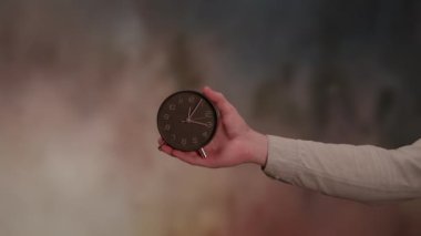 Zarif, zarif bir saat, güzel bir şekilde bulanık, sanatsal bir arka plana ayarlanmış bir elle tutulur.
