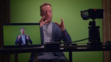 Bir adam yeşil ekran arkaplanı önünde konumlandırılırken bir video sunumunu kaydetmekle meşgul