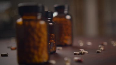 Vitaminlerle dolu çeşitli şişeler ve bir sürü hap dikkatsizce ahşap masaya saçılmış.