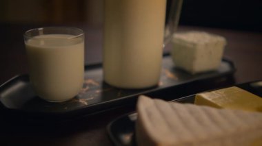 Süt, peynir ve tereyağı gibi taze süt ürünleri koyu ahşap bir masaya dizilmiştir.