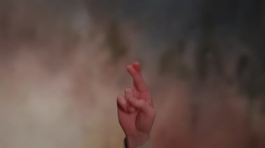 Parmakları sıkıca çaprazlanmış bir elin yakın çekimi çarpıcı bir arka plana karşı umudu ya da şansı simgeler.