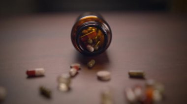 Ahşap bir yüzeye yayılmış çeşitli kapsüllerle dolu dökülmüş bir ilaç şişesinin detaylı bir yakın plan görüntüsü.