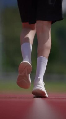 Canlı ve dinamik bir atletizm pistinde yürüyen bir sporcunun bacaklarını gösteren yakın plan bir görüntü.