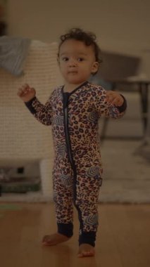 Sevimli genç bir çocuk neşeli pijamalarıyla neşeli bir şekilde ayakta duruyor, sıcak ve kapalı bir ortam sergiliyor.