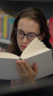 Huzurlu bir kütüphane ortamında oturmuş kitap okumaya dalmış genç bir kadın,