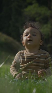 Neşeli ve neşeli bir çocuk, güneşli bir gökyüzünün altında yumuşak, yeşil çimenlerde otururken doğayı keşfetmekten zevk alır.