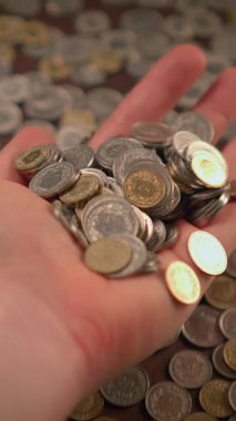 Çeşitli madeni paraları sıkıca kavrayan, zenginliği ve çeşitli finansal işlemleri sembolize eden bir el.