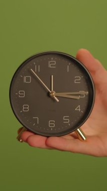 Şık, şık, modern bir saat, canlı yeşil bir arkaplan karşısında tam zamanını gösteriyor.